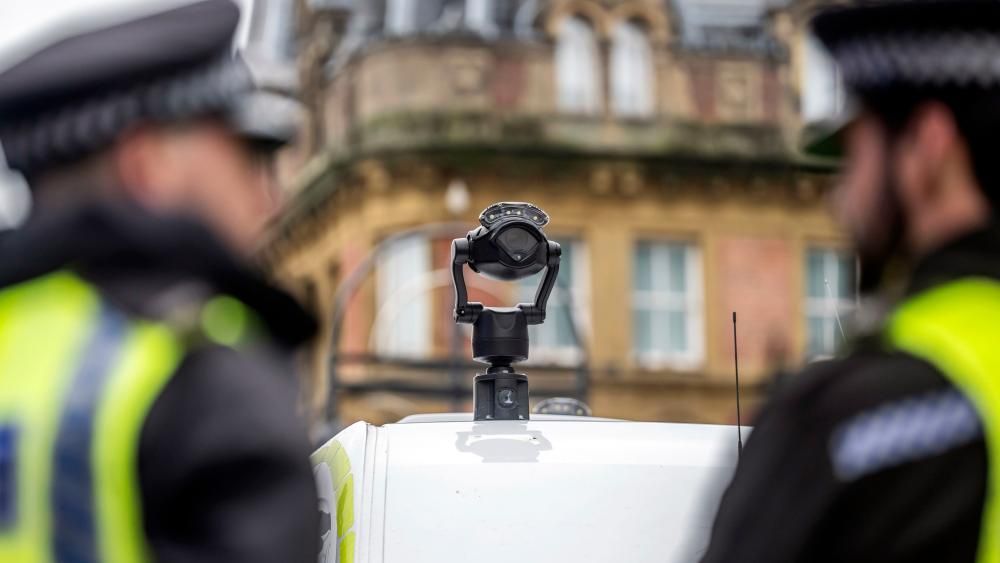 2 UK police officers staning in front of a facial recognition camera 